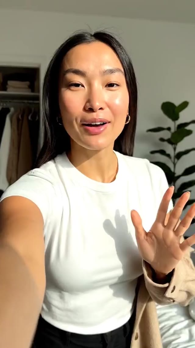 A creator in a bright bedroom waving to the camera, putting on a beige wool overshirt, turning to show it and giving a thumbs up